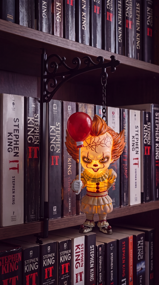 Horror clown book nook light with red balloon glowing warm amber, hanging between books on a dark shelf